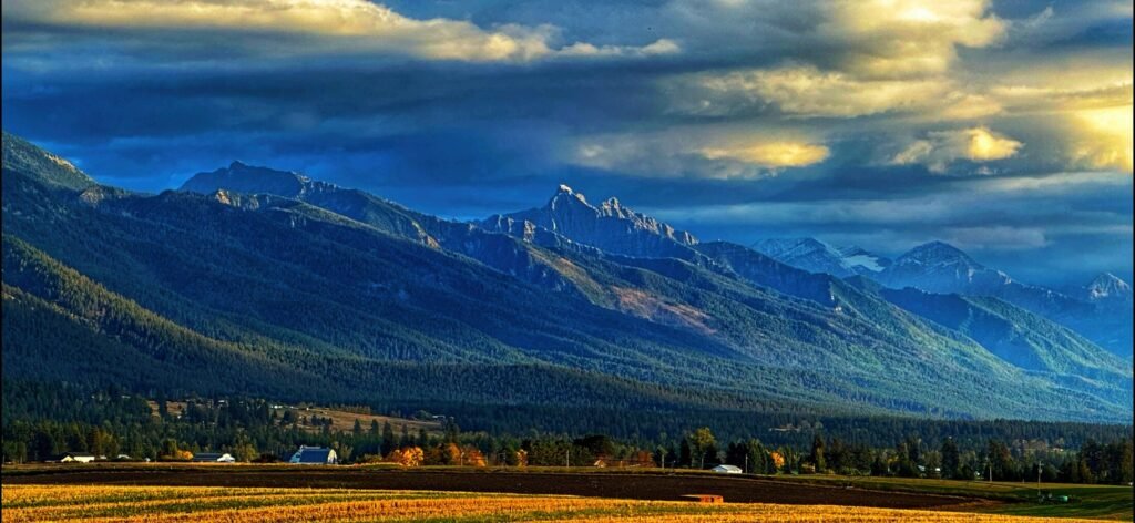 Blue mountain range above a golden valley beneath layered clouds and breaks of sunlight.