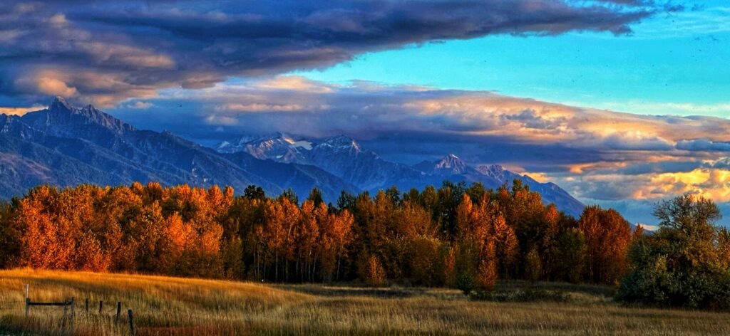 Orange autumn trees glow beneath a mountain range and layered blue-gray clouds.