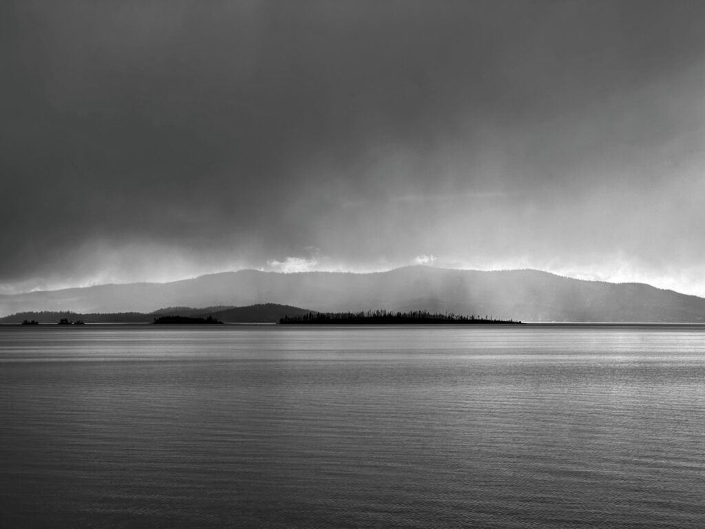 Black-and-white rain bands descend over a distant mountain ridge and calm water.