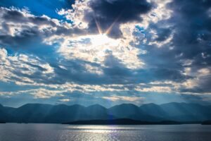 Sunlight breaking through dramatic clouds above mountains and water