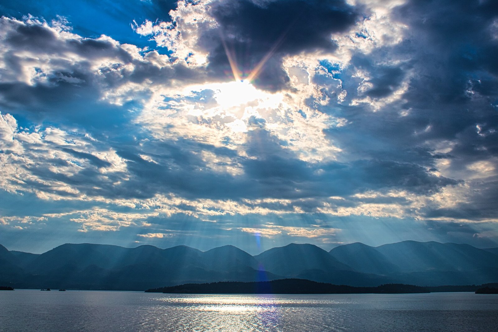 Sunlight breaking through dramatic clouds above mountains and water